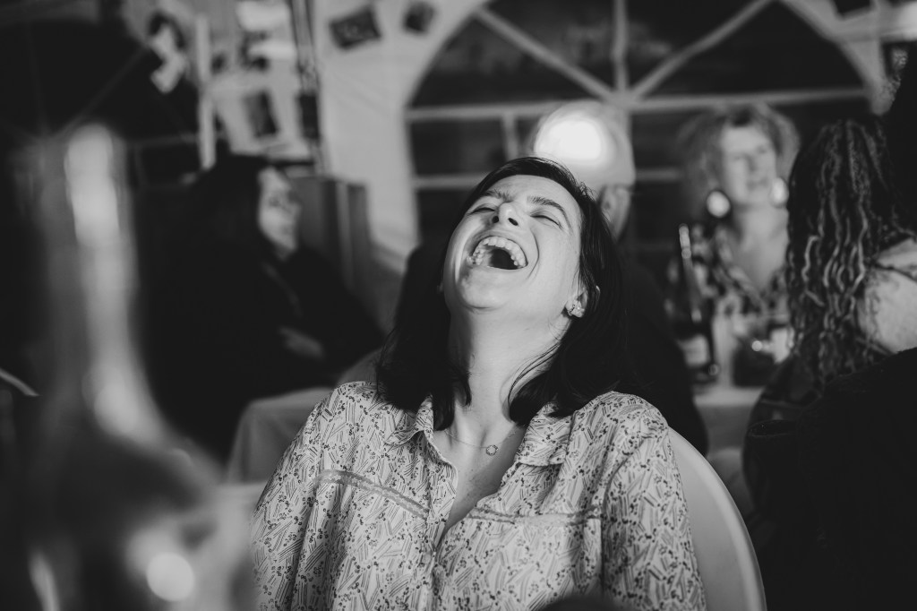 Femme riant aux éclats, entourée d'amis lors d'une soirée conviviale, capturant un moment de joie authentique.